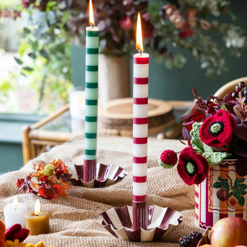 A red and white striped advent candle with numbered bands from 1 to 23, standing in a matching red and white striped cup holder with a red ribbon bow, set against a teal background.