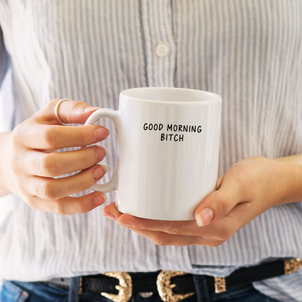 Person holding a white mug with 'GOOD MORNING BITCH' text