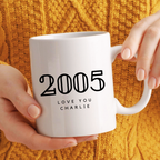 White mug with '2005 LOVE YOU CHARLIE' text held by a person against a yellow textured background