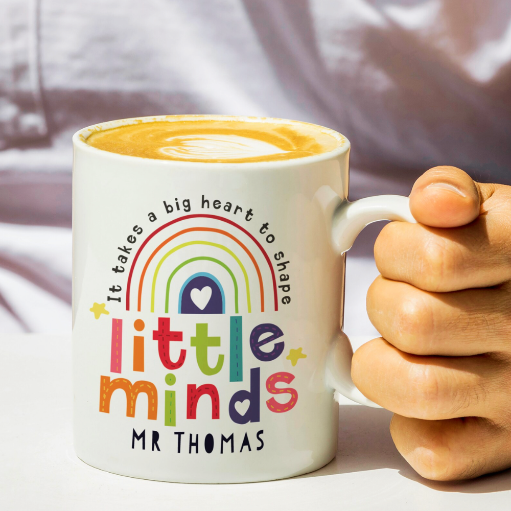 Personalised Little Minds teacher mug held in hand with latte showing Mr Thomas name on front with rainbow design