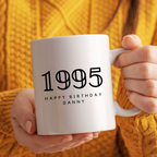 Person holding a white mug with '1995 Happy Birthday Danny' text against a yellow textured background