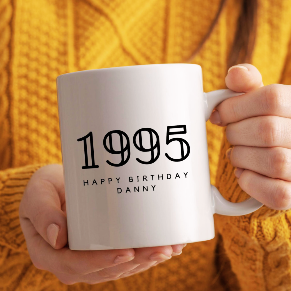 Person holding a white mug with '1995 Happy Birthday Danny' text against a yellow textured background