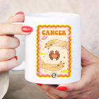 White mug with Cancer zodiac design held by a person with red nail polish.