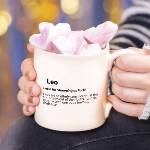 Person holding a mug with pink heart-shaped objects and a humorous definition of 'Leo' printed on it.
