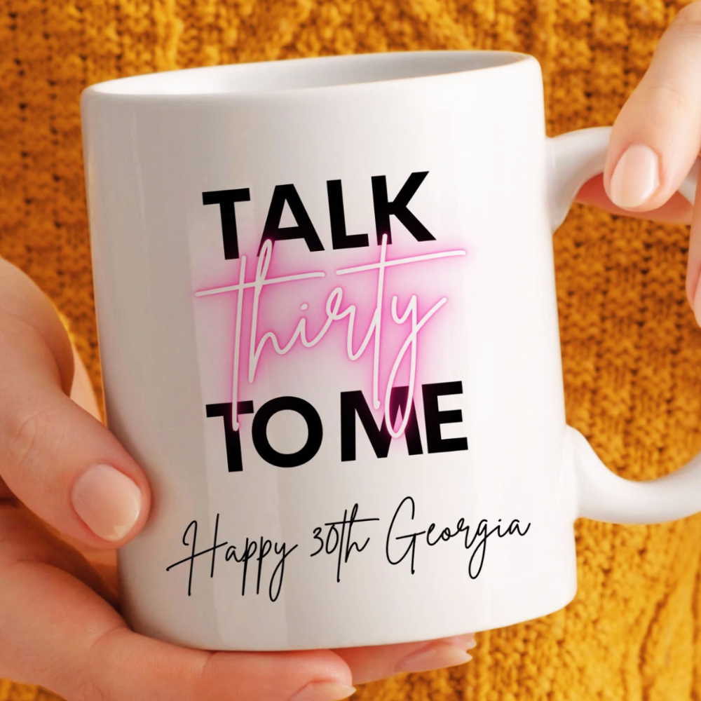 White mug with 'Talk thirty to me Happy 30th Georgia' text held by a hand against an orange textured background