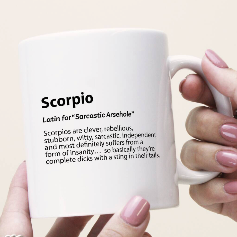 White mug with Scorpio definition text held by a hand with pink nail polish.