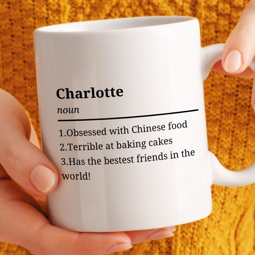 White mug with text definition of 'Charlotte' held by a hand against an orange background