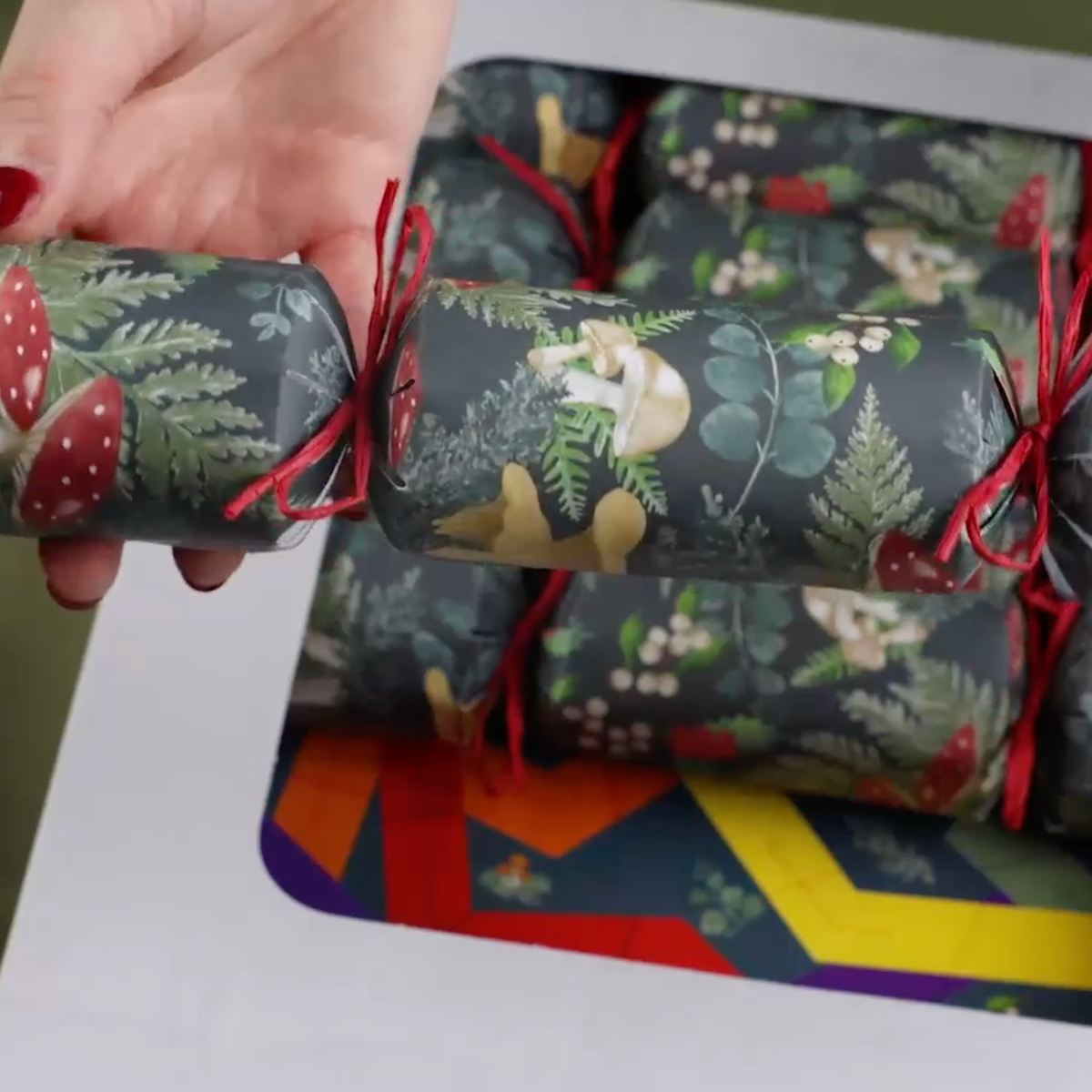 Close-up of a forest green Christmas cracker with toadstools, foliage and red ties