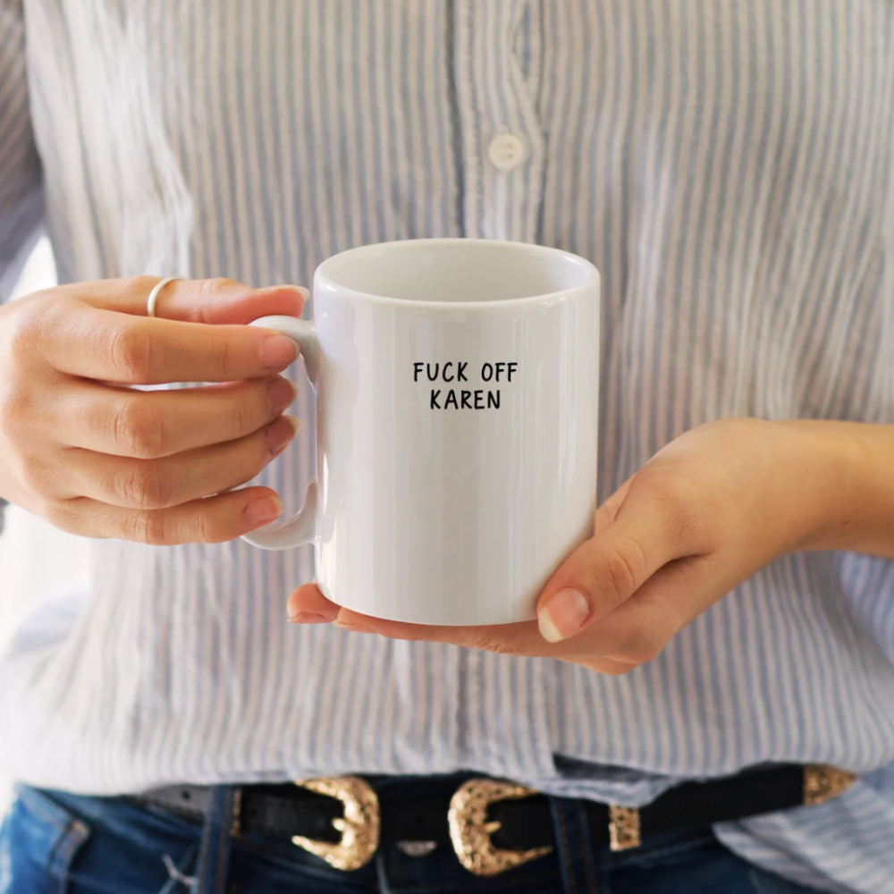 Person holding a white mug with text, wearing a striped shirt.