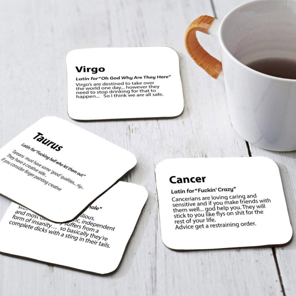 Set of four coasters with zodiac-themed text on a wooden surface with a mug.