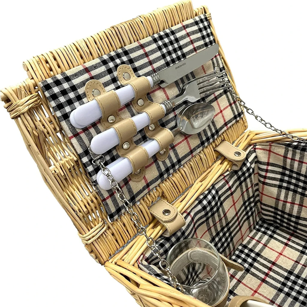 A wicker picnic basket with a beige, black, and red plaid fabric lining, shown open to display a matching cutlery set with white handles and a glass cup inside.