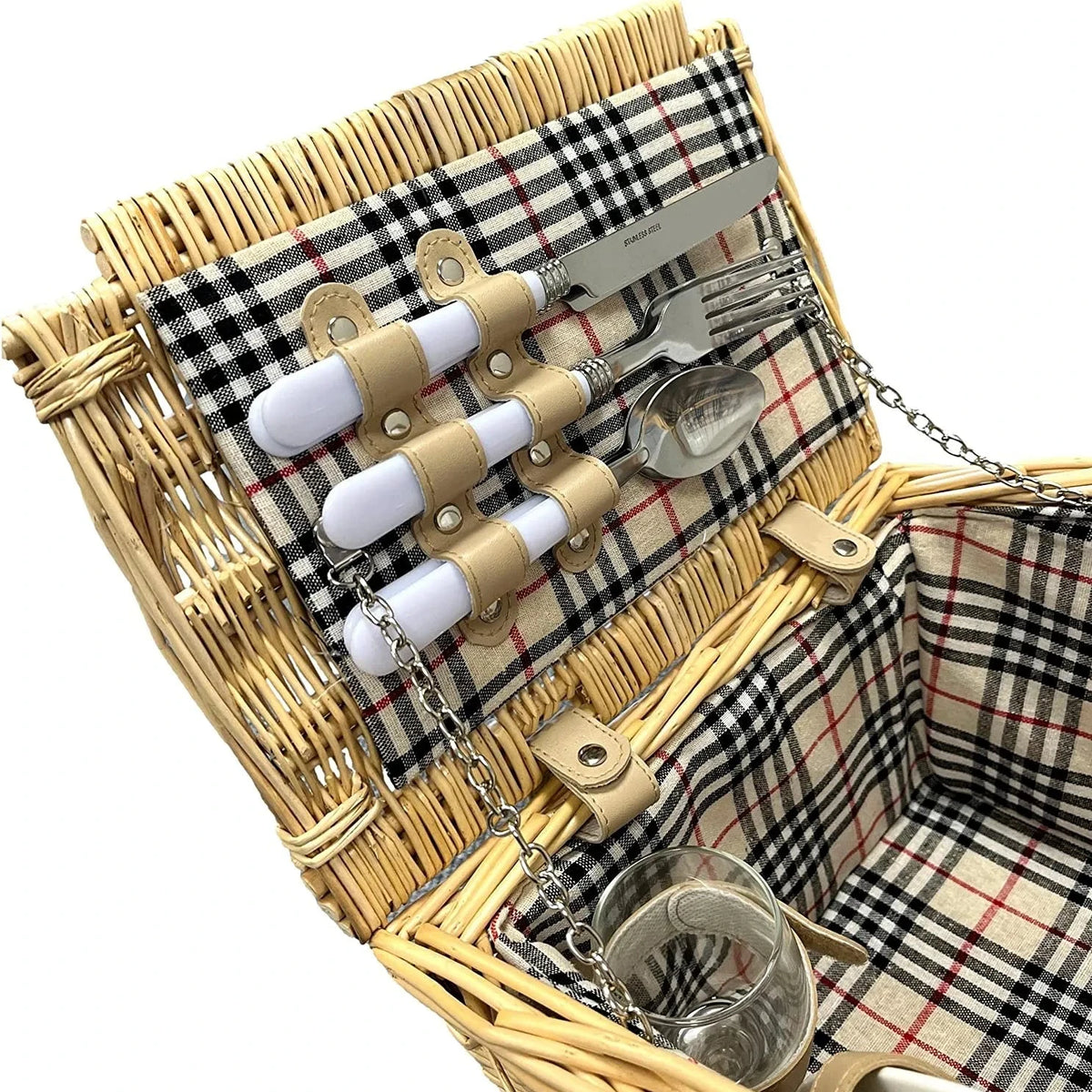 A wicker picnic basket with a beige, black, and red plaid fabric lining, shown open to display a matching cutlery set with white handles and a glass cup inside.