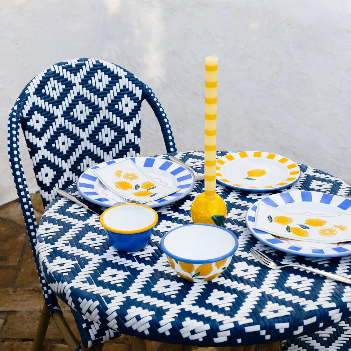 Lemon Stripe Dinner Candle in a yellow lemon ceramic candleholder on a teal striped tablecloth against a yellow wall