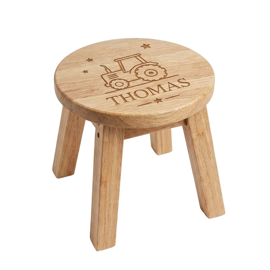 A small round wooden stool with four legs, featuring an engraved tractor design and the name 'THOMAS' on the seat, shown on a clean white background.