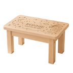A small wooden children's stool or table with engraved personalisation reading 'RONNIE' and 'touch for the stars,' shown in a nursery-like room on a star-patterned rug.