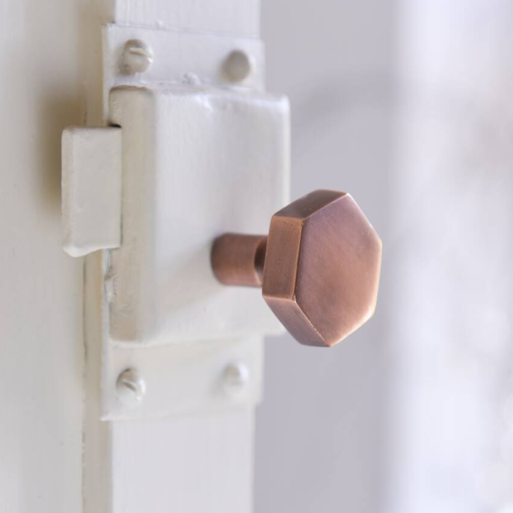A close-up of a hexagonal copper-colored metal door knob mounted on a white door latch.