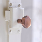 A close-up of a hexagonal copper-colored metal door knob mounted on a white door latch.