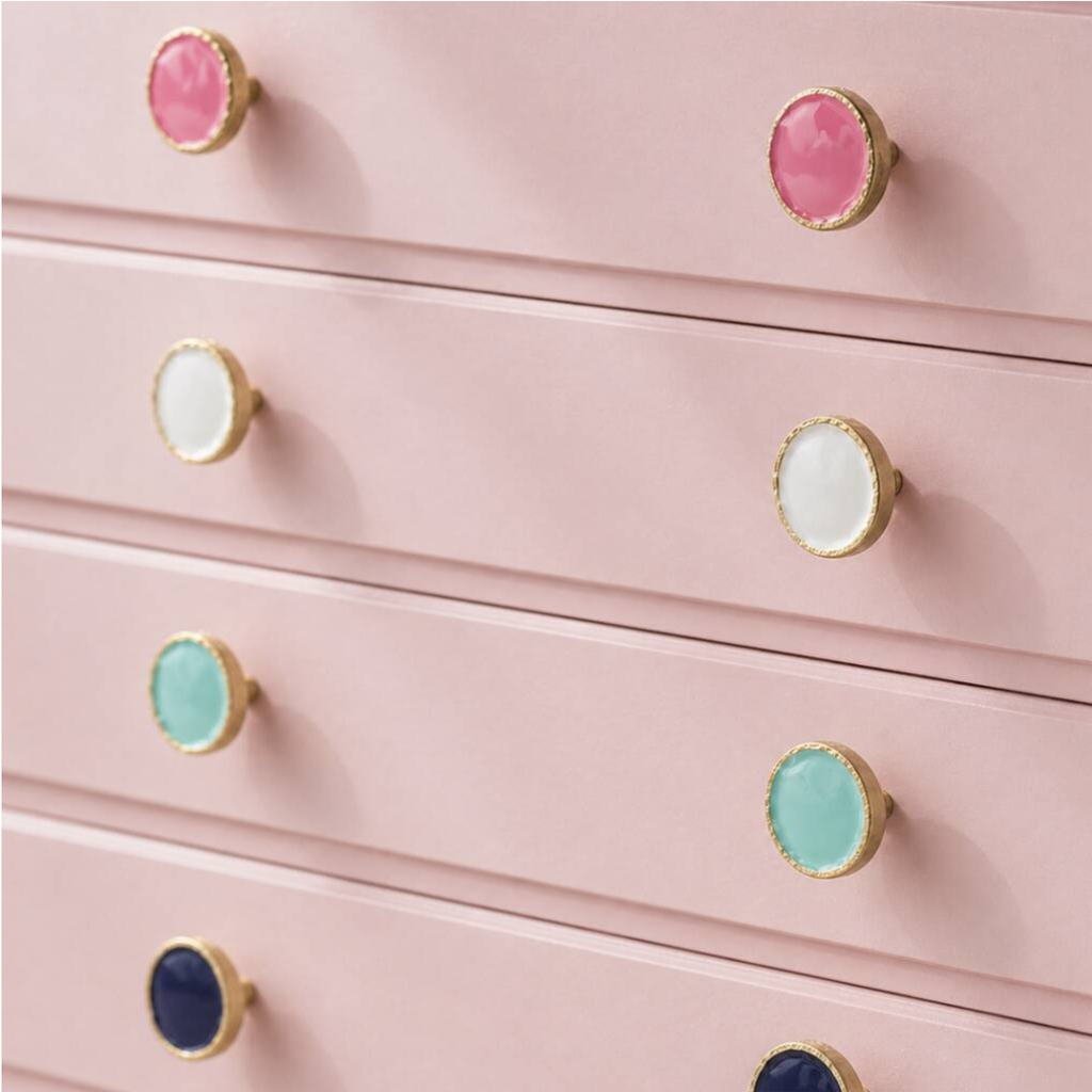 A close-up of a pink dresser with multiple drawers, each fitted with round gold-tone knobs featuring colorful centers in pink, white, mint, blue, and light aqua.