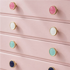 A close-up of a pink dresser with multiple drawers, each fitted with round gold-tone knobs featuring colorful centers in pink, white, mint, blue, and light aqua.