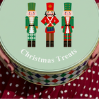 A round tin of Christmas treats held by a person wearing a red and white polka dot dress. The lid is pale mint green with white text reading 'Rowan & Hallies Christmas Treats' and an illustration of three nutcracker figures in green, red, and black.