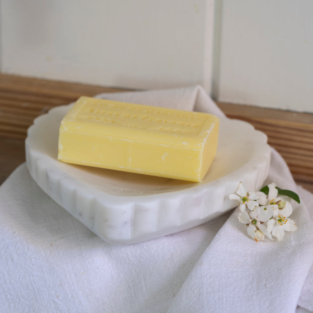 Marble Heart Dish styled on a white linen cloth with a yellow soap bar and white blossom flowers on a wooden surface