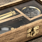 A wooden keepsake box with a clear glass lid, featuring engraved text and vintage-style nautical instruments inside, including a brass compass and a small telescope, shown on a rustic wooden surface.