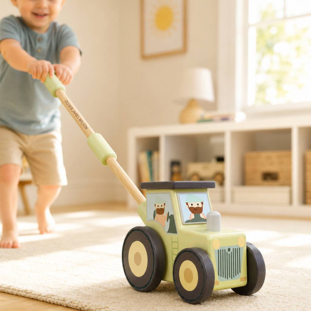 A child pushes a wooden toy tractor on a light rug in a bright, modern room. The toy tractor is light green with black and beige wheels and cartoon animal windows.