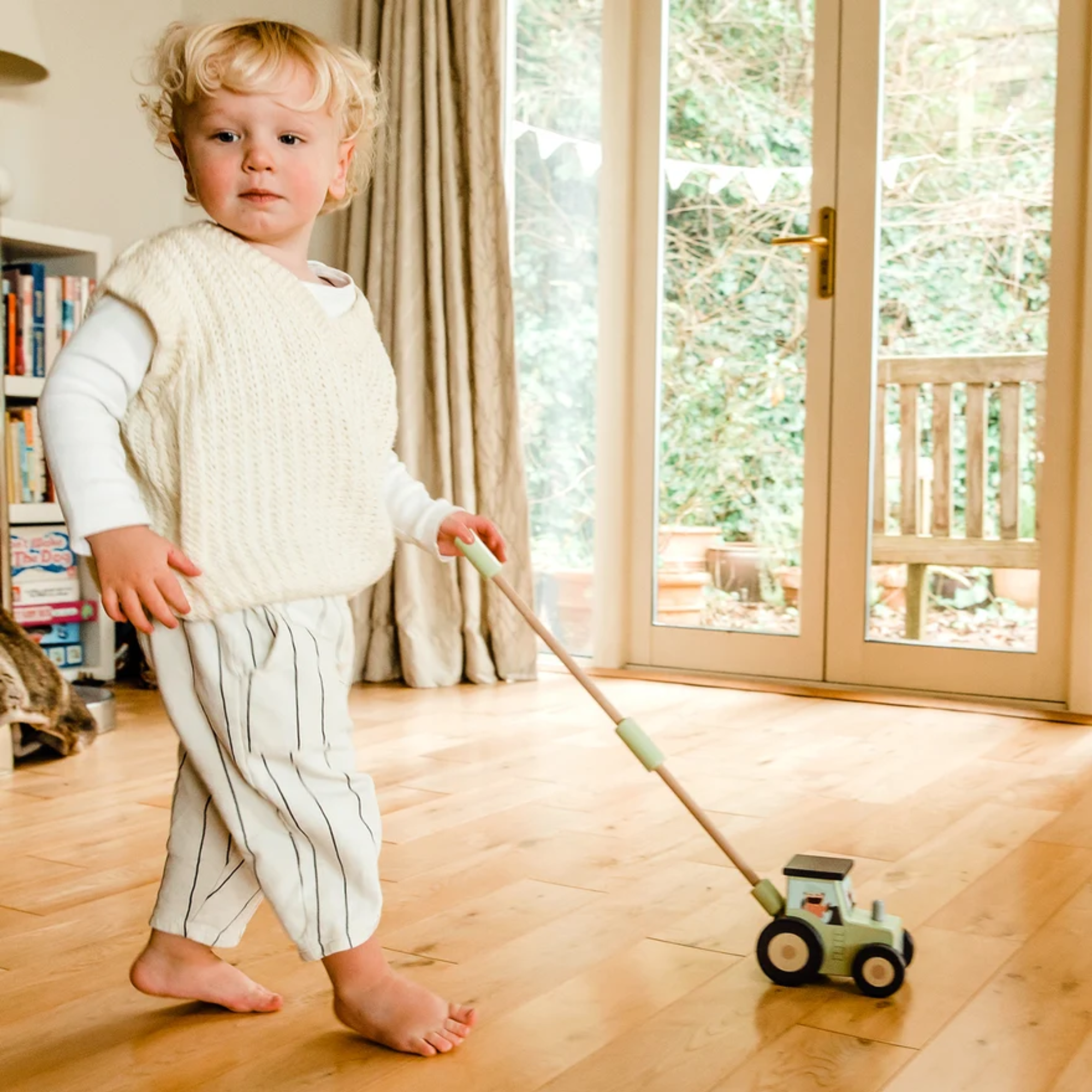 Child playing with a toy on a wooden floor in a room with large windows.