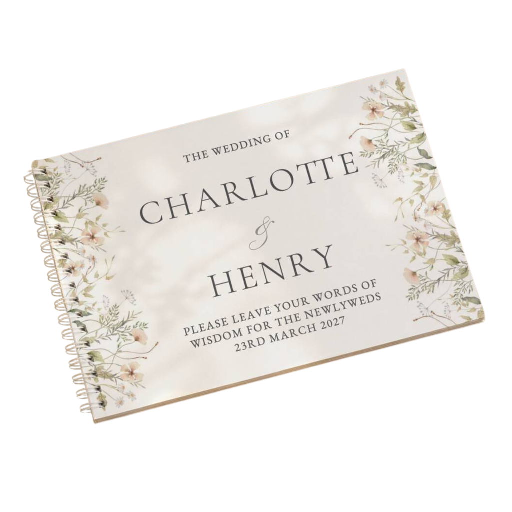 A spiral-bound wedding guest book with a cream-colored cover decorated with delicate floral illustrations on the left and right sides. The text on the cover reads 'THE WEDDING OF CHARLOTTE & HENRY' with placeholder wedding text below, shown on a clean white background.