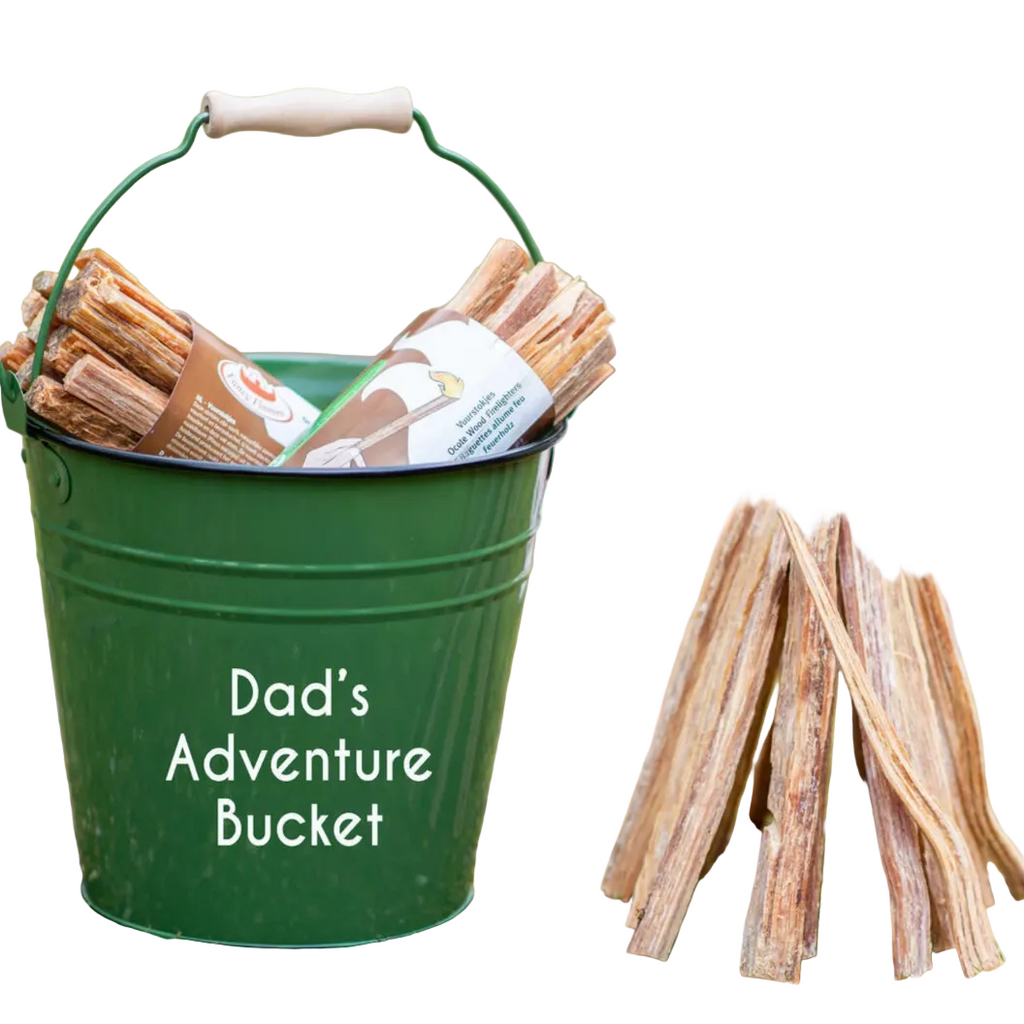 Green bucket labeled 'Dad's Adventure Bucket' with firewood and a small wooden campfire structure outdoors.