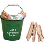 Green bucket labeled 'Dad's Adventure Bucket' with firewood and a small wooden campfire structure outdoors.