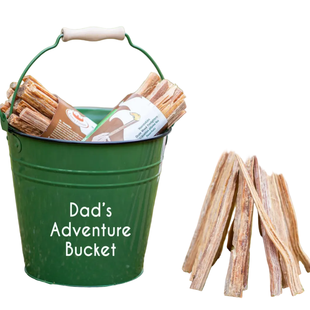 Green bucket labeled 'Dad's Adventure Bucket' with firewood and a small wooden campfire structure outdoors.