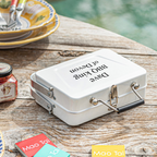 White lunch box with engraved text on a wooden table with food items in the background
