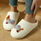 A person wearing fluffy off-white slip-on slippers with colorful embroidered dog illustrations, shown with blue jeans on a wooden floor.