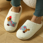 A person wearing fluffy off-white slip-on slippers with embroidered teddy bear designs, paired with blue jeans, standing on a light wood floor.