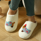 A person wearing fluffy off-white slip-on slippers with embroidered cartoon motifs on the top, paired with blue jeans, standing on a light wood floor.