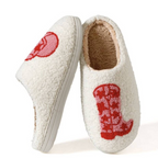 A pair of off-white sherpa slip-on slippers with red embroidered boot motifs on the sides, displayed against a clean white background.