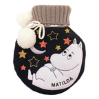 A round black knit hot water bottle featuring a white embroidered Moomin character on the front, surrounded by embroidered stars in gold, orange, and red. The bottle has a gray ribbed knit neck with two white pom-poms attached by white cord.