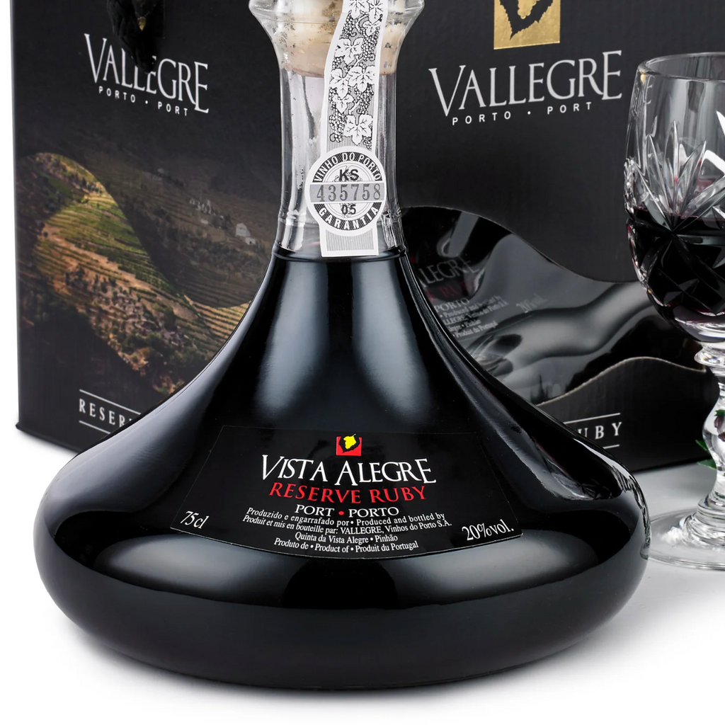 Vista Alegre Reserve Port wine bottle with its black presentation box and a crystal glass of dark red wine, shown on a white background with a grape garnish.