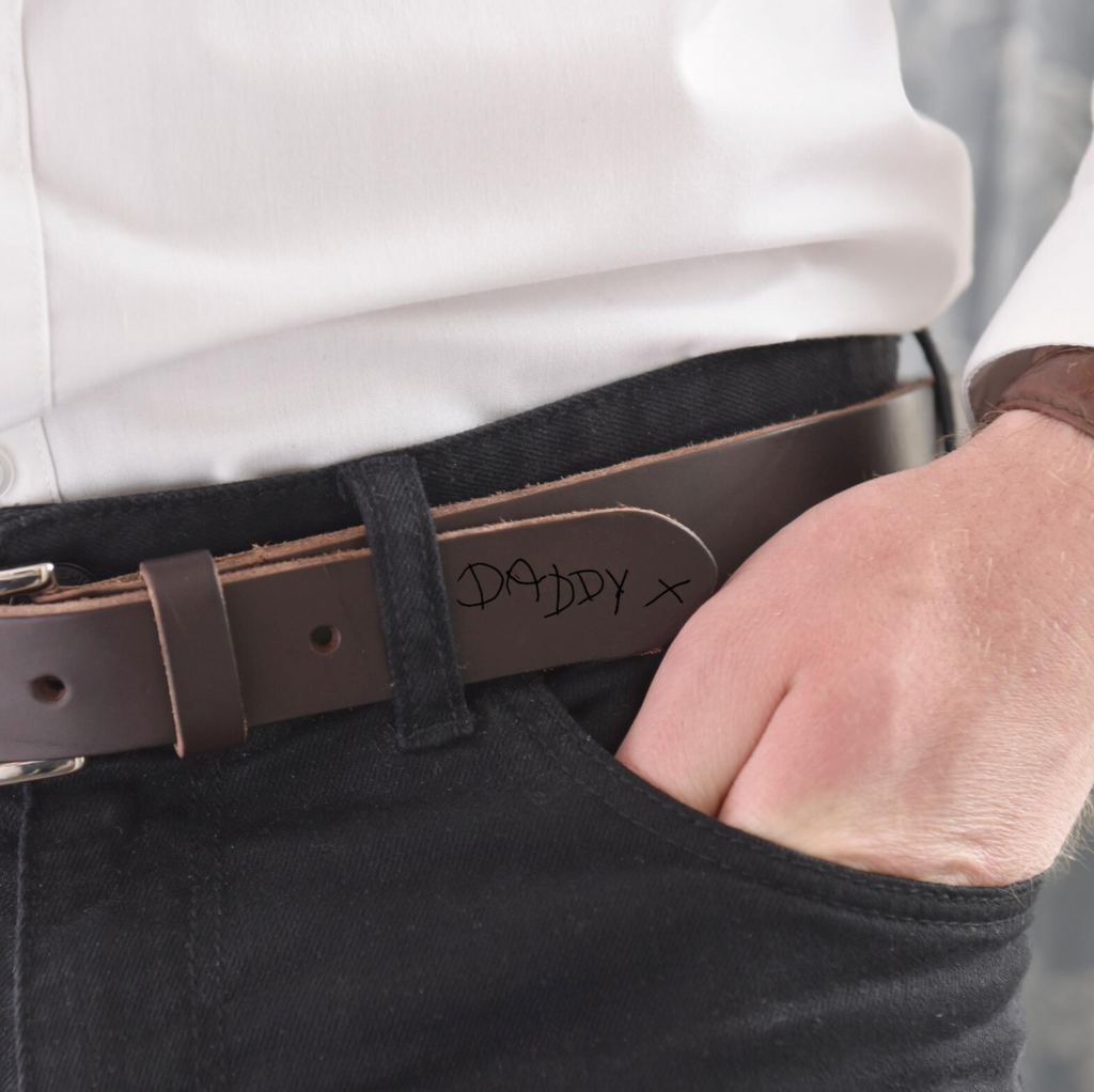 Brown belt with 'Daddy X' engraving worn by a person in a white shirt and black pants.
