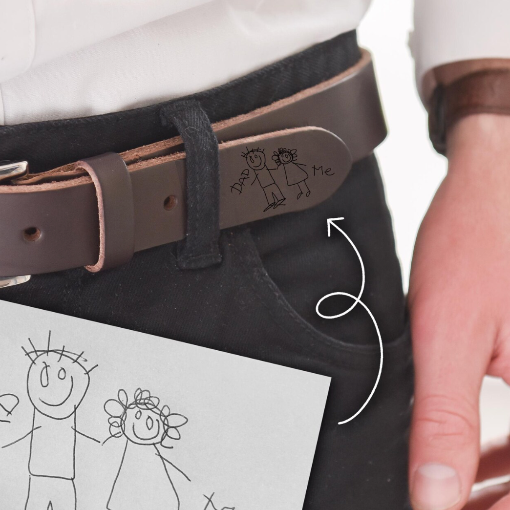 Person wearing a belt with a hand-drawn design, holding another piece of paper with similar drawings.
