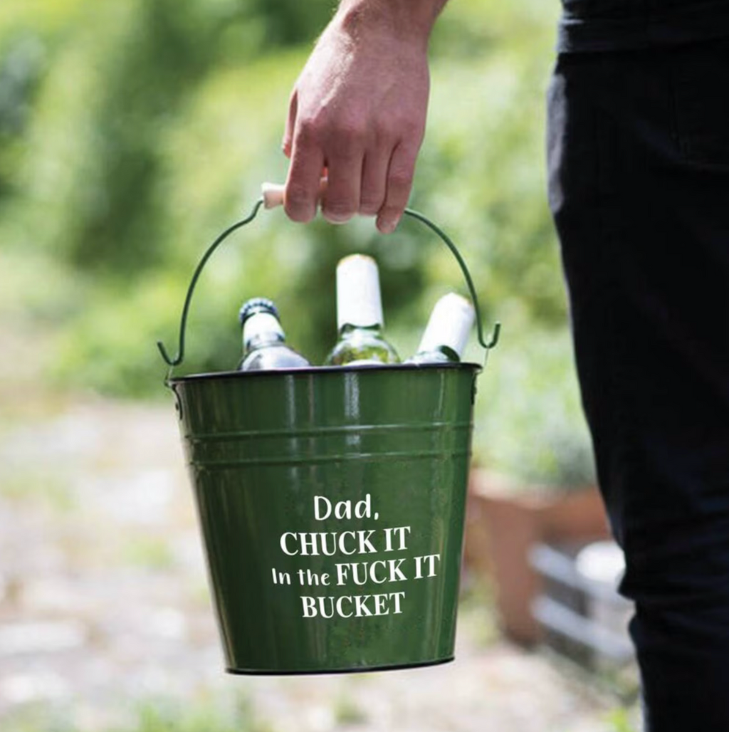 Person holding a green bucket with bottles and humorous text outdoors