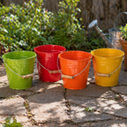 Four colorful buckets (green, red, orange, yellow) on a stone surface with plants in the background.