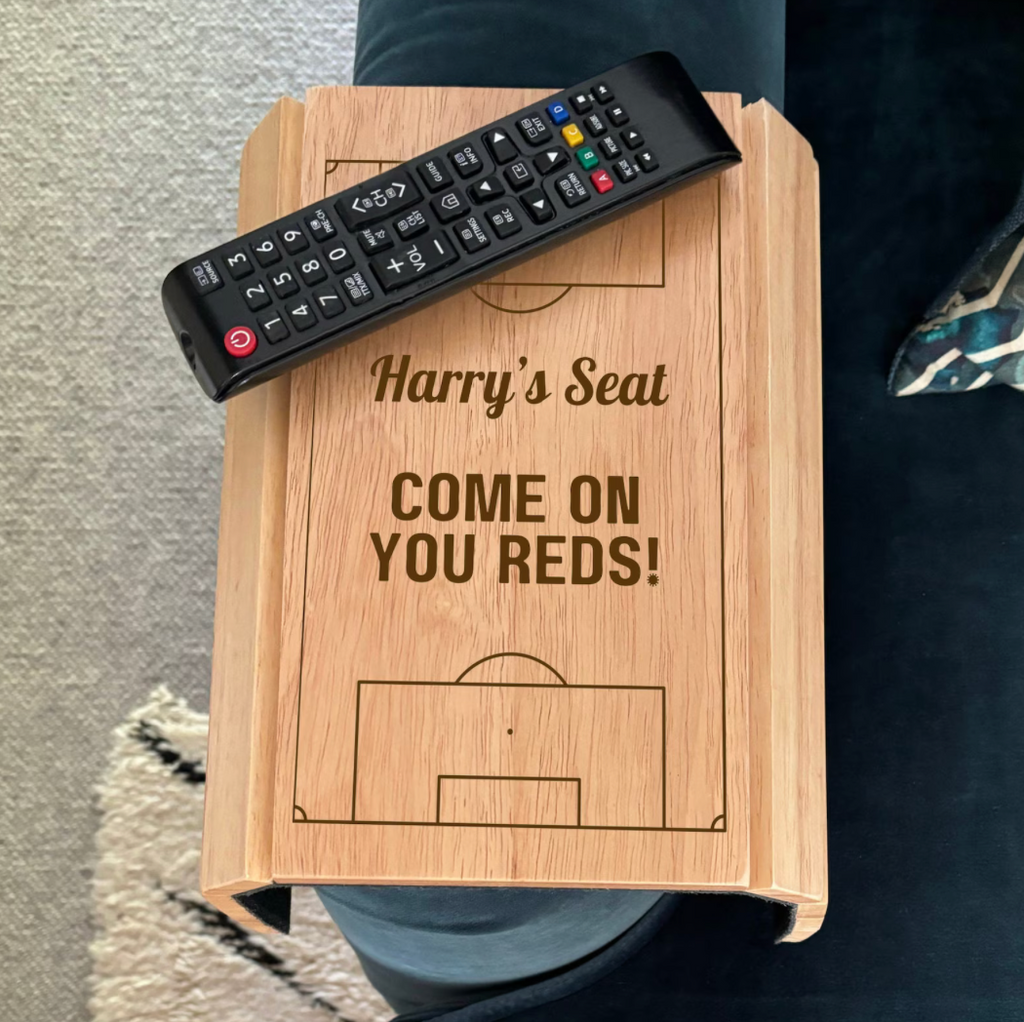 Wooden stool with 'Harry's Seat' and 'Come on You Reds!' text, remote control on top.