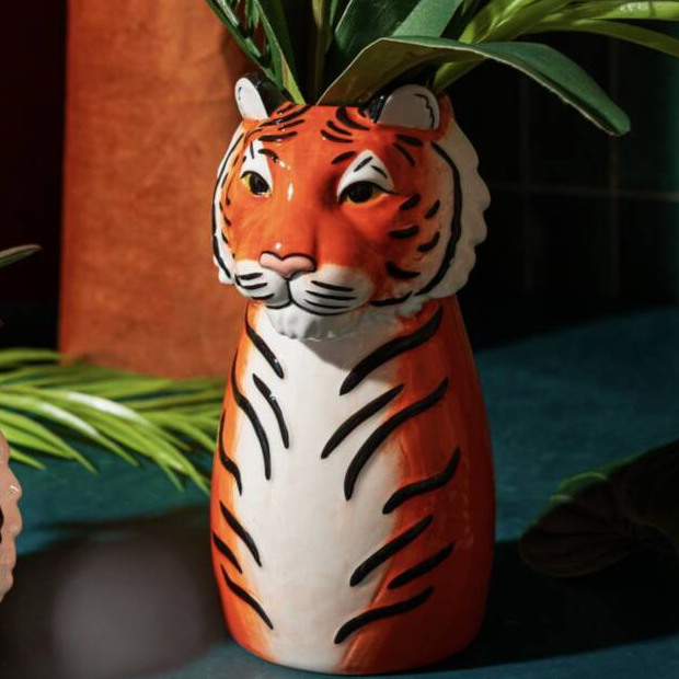 Both ceramic tiger planter and vase displayed together with plants in a warm jungle-inspired setting