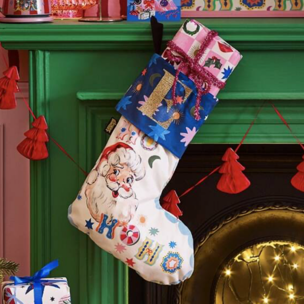 Embroidered Santa Velvet Stocking hanging on a green fireplace mantel with Christmas gifts