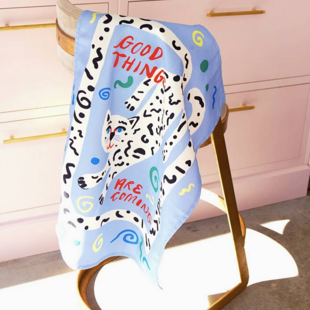 Good Things Are Coming Tea Towel draped over a gold chair in a pink kitchen in sunlight