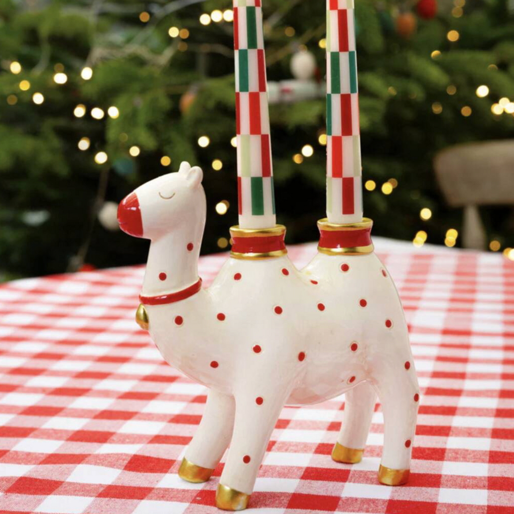 Close up of Ceramic Camel Candle Holder on a red surface with striped taper candles in the humps