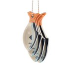 Sardine Ceramic Measuring Spoons hanging on silver ball chain on a marble surface next to blueberries, rosemary and a whisk