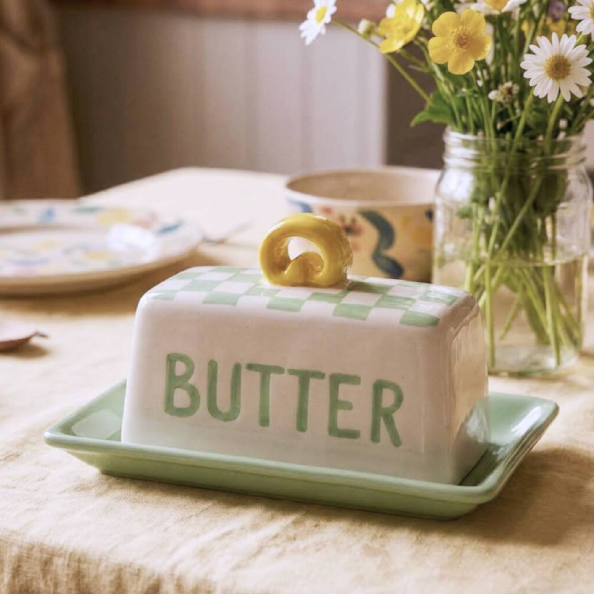 Hand Painted Green Check Butter Dish styled on a linen tablecloth with yellow wildflowers and a floral mug in the background